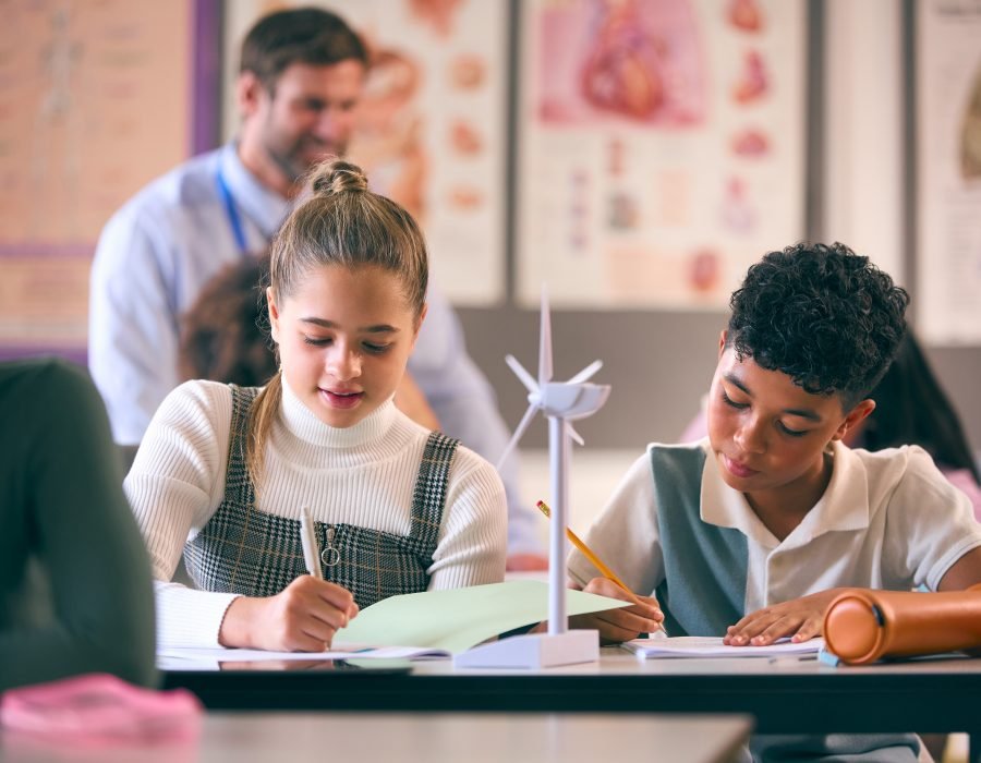 Secondary Or High School Students Studying Wind Turbines In Science Class With Teacher In Background